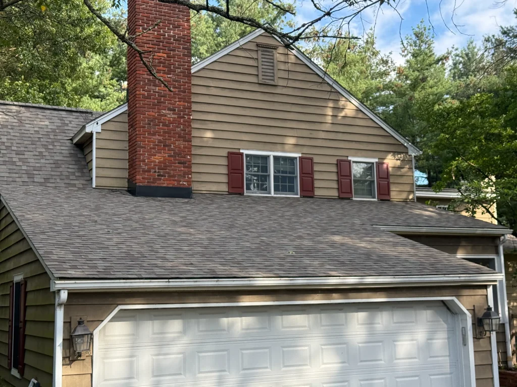 Asphalt shingle roof replacement with new chimney flashing on a home with tan siding and white gutters
