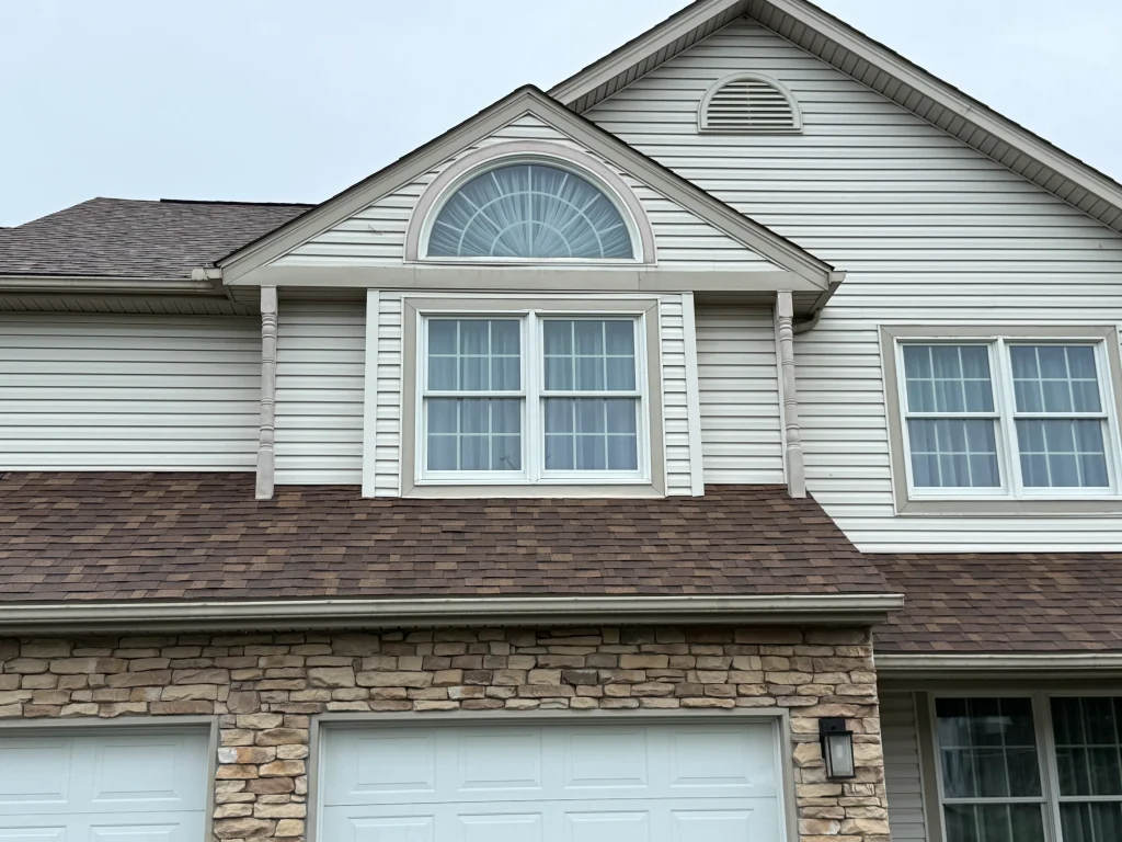 Brown standing seam metal roof with snow guards and matching gutters and downspouts on a wooded residential property