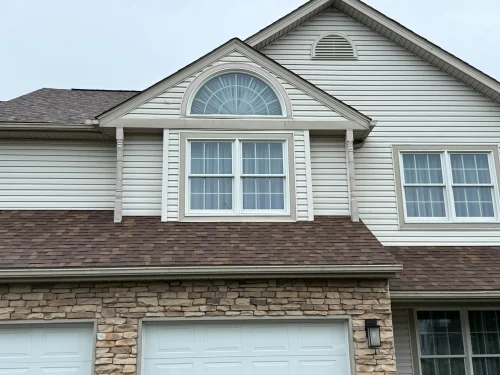 Brown standing seam metal roof with snow guards and matching gutters and downspouts on a wooded residential property