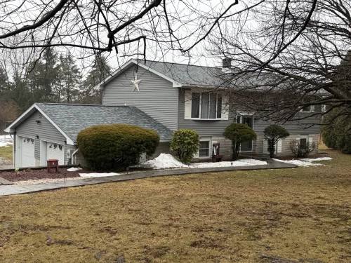 Split-level home with a new gray asphalt shingle roof, gray vinyl siding, and attached two-car garage