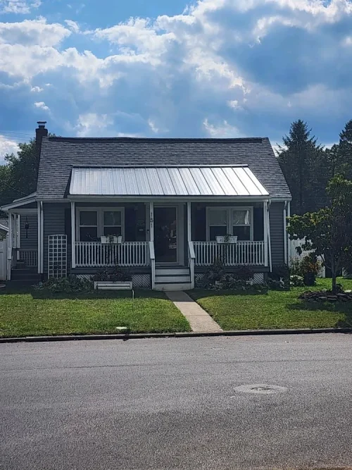 Front view of a home with a charcoal asphalt shingle roof and a silver standing seam metal porch roof