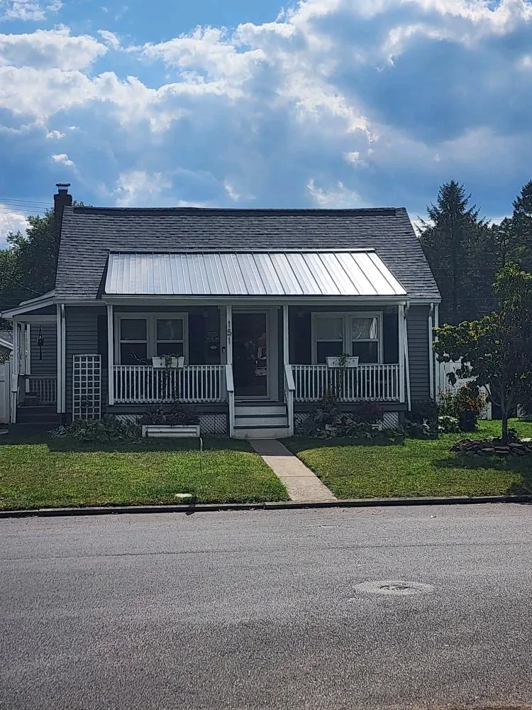 Front view of a home with a charcoal asphalt shingle roof and a silver standing seam metal porch roof
